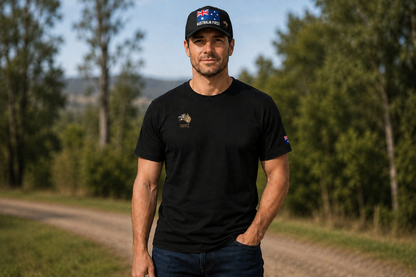 A man wearing The Australian Lobby Group black short-sleeve t-shirt and black trucker cap with the AUSTRALIA FIRST Australian flag graphic, standing outdoors on a country road.